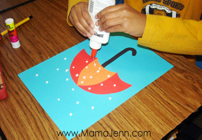 child's hand putting drops of glue on construction paper umbrella craft
