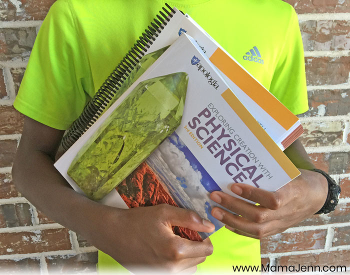 boy holding Apologia Physical Science Student Notebook and textbook